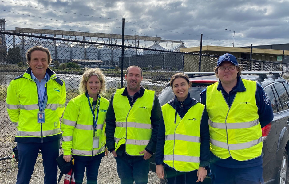 A group of five people wearing hi-vis yellow jackets, standing alongside the Port of Melbourne.