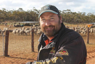 Jason Marwood standing with a fenced paddock of sheep behind him