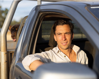 Man in ute, elbow out, dog peeking out from behind