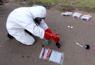 An inspector in a hazard suit gathers evidence.