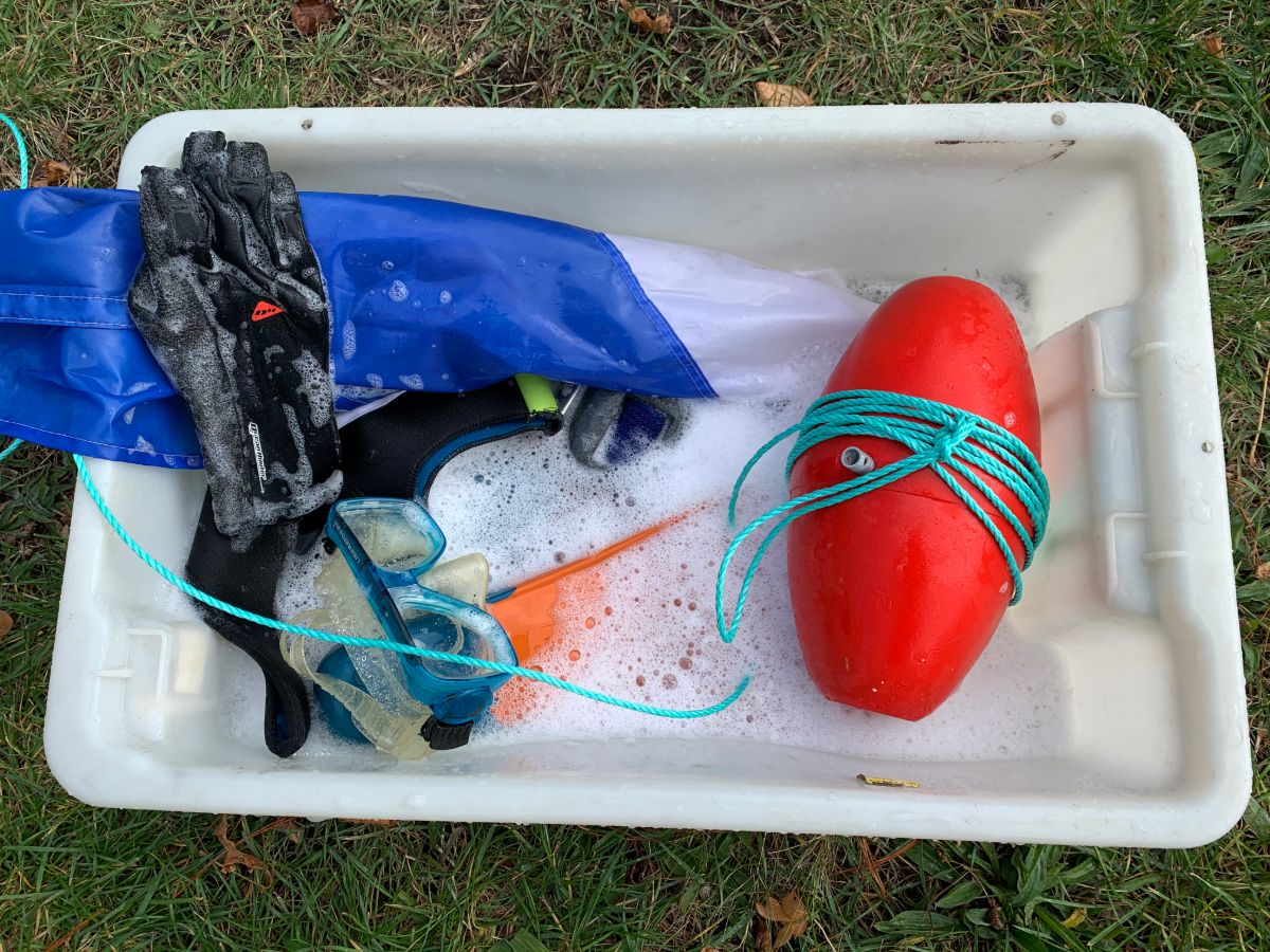 Wetsuits, gloves and other diving equipment in a tub of soapy water.