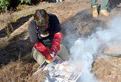 Farmer with mask and rubber gloves using newspaper to fan smoke over a warren