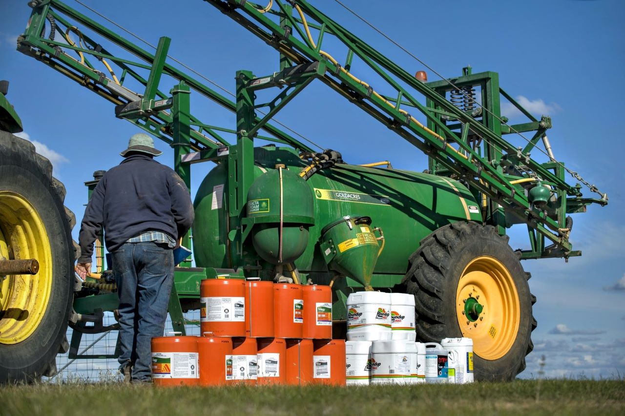 Image shows a farmer standing near a tractor. The farmer is preparing to conduct agricultural chemical spraying.