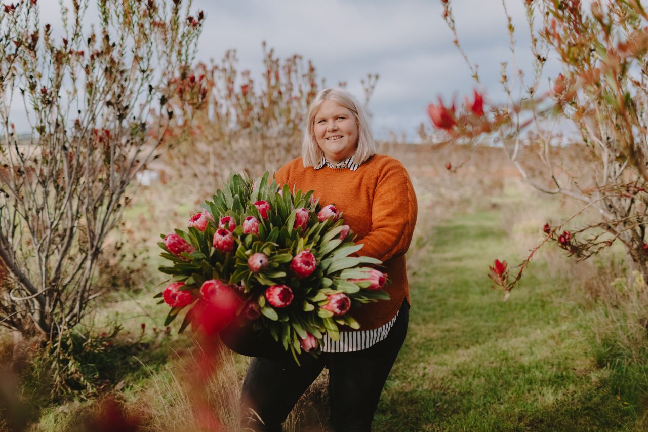 Photo shows AgrFutures Australia award winner Nikki Davey carrying a large bunch of red flowers.