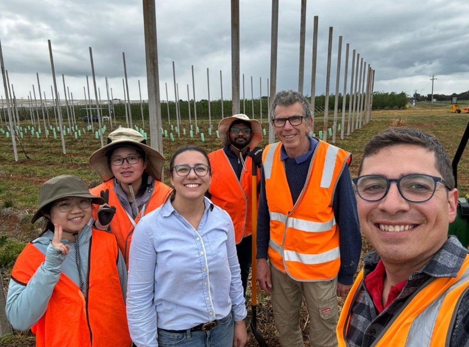 Six people in front of planted crops, five of them in hi-vis vests.