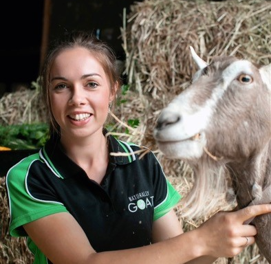 Orianna-Edmonds with a goat in a shed with haystack in the background.