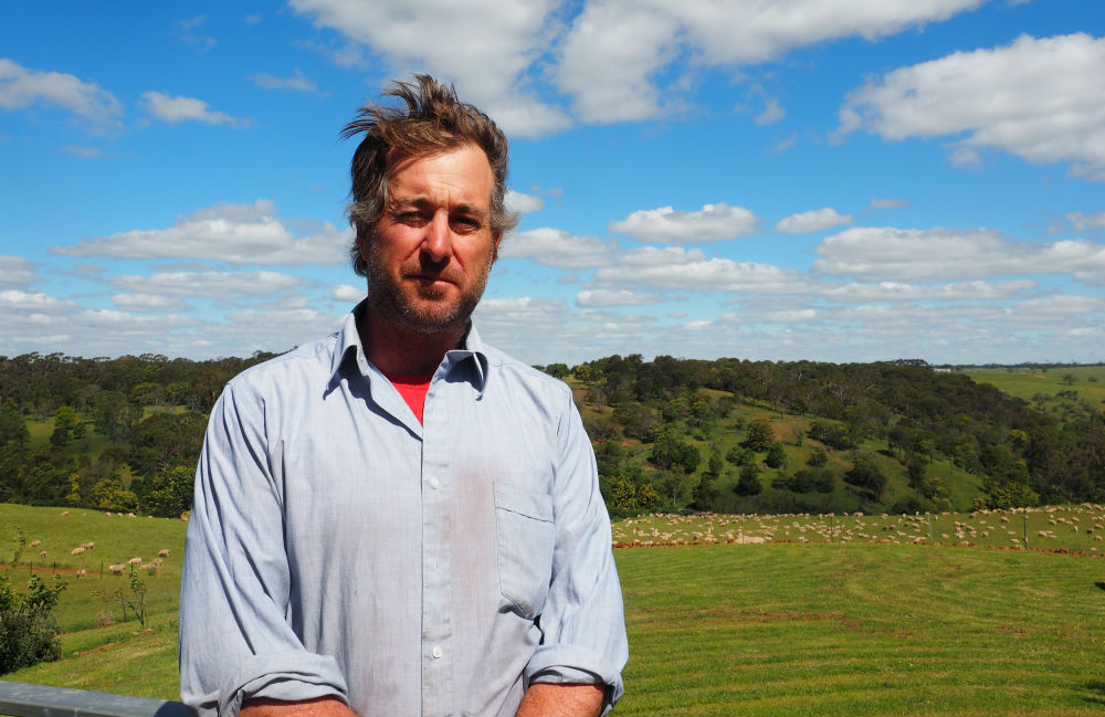 Farmer Andrew Edgar pictured on his farm with sheep and trees in the background