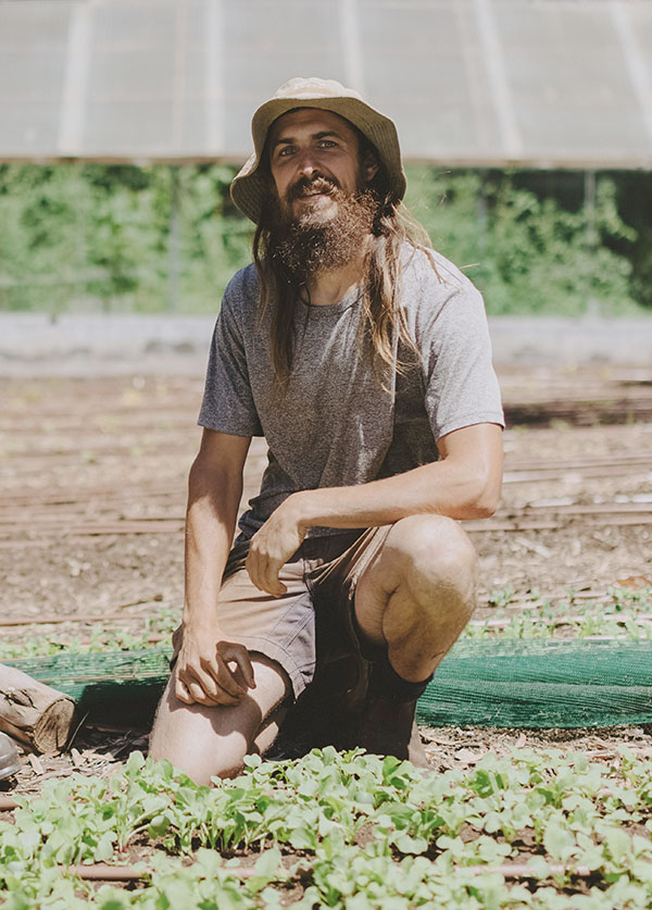 Joash Williams on one knee among a crop of shoots in a hat on sunny day