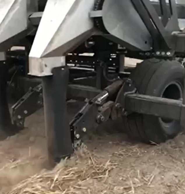 Photo of the lower part of a subsoil amelioration machine in operation with hydraulic breakouts and a large flexible boot to reduce bridging. 
