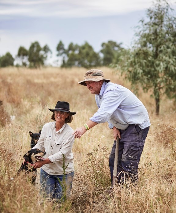 Jo and Greg Bear with their dogs in an area of their farm where tree planting has occurred. Image: Woolmark (https://www.woolmark.com/) Jo and Greg Bear with their dogs in an area of their farm where tree planting has occurred.
