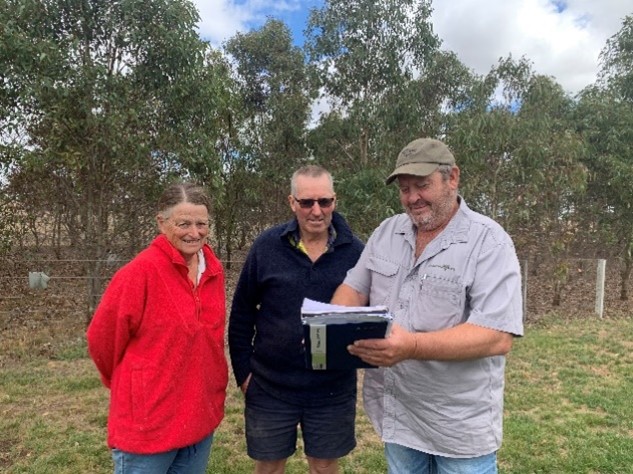 3 people looking at a notebook with trees behind them