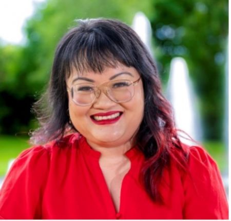 A photograph of a woman in a red shirt smiling at the camera