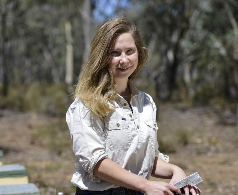 Millie Enbom-Goad standing on a field in front of beehives.